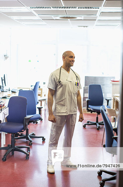 Volle Länge des mittleren erwachsenen männlichen Arztes  der weg schaut  während er in der Klinik steht.
