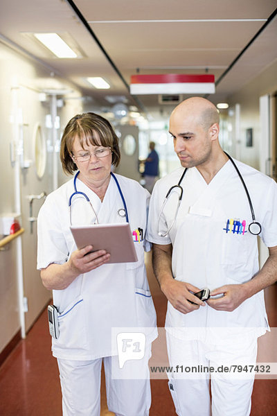 Doctors using digital tablet while standing in hospital corridor