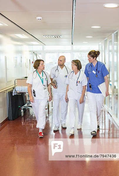 Team of four doctors discussing while walking in hospital corridor