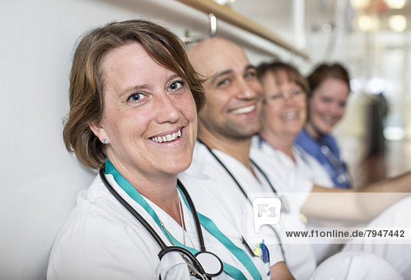Portrait of happy mature female doctor with colleagues leaning on wall in hospital