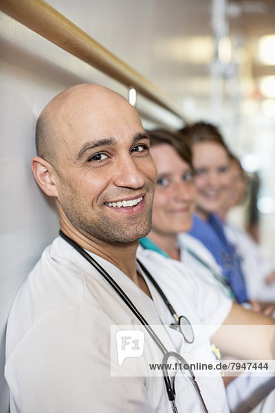 Porträt eines mittelgroßen männlichen Arztes mit Kollegen an der Wand im Krankenhaus