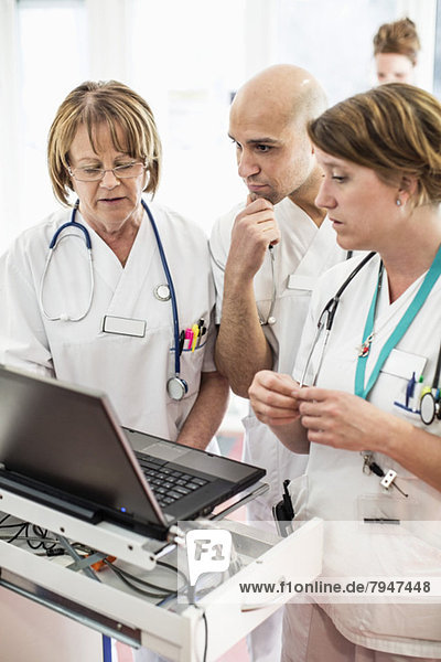 Arzt und Ärztin diskutieren über Laptop mit Kollegen im Krankenhaus