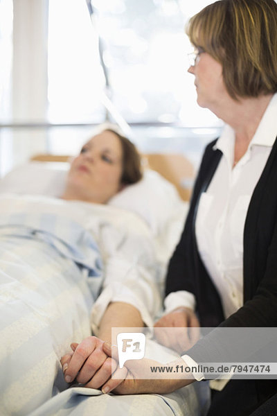 Seniorin mit der Hand der Tochter auf dem Bett liegend in der Krankenstation