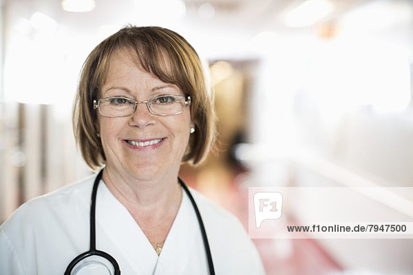 Portrait of happy senior female doctor standing in hospital