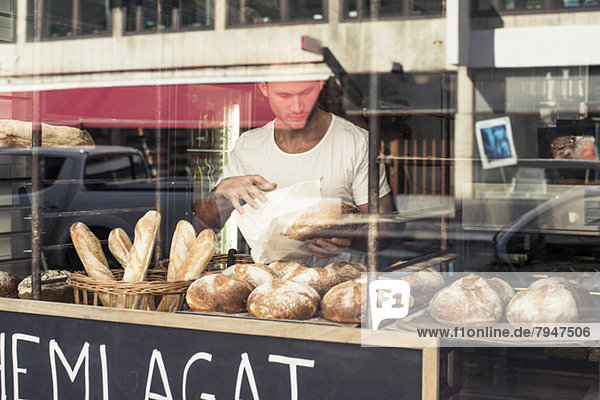 View of mid adult male owner working at bakery through display cabinet