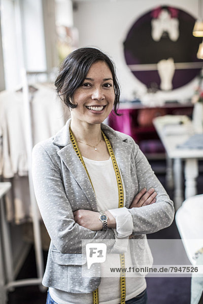 Porträt einer fröhlichen Modedesignerin  die im Atelier gekreuzt steht.