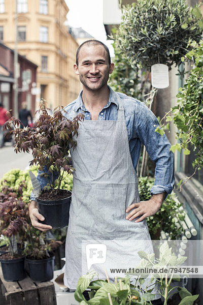 Portrait of confident male florist holding potted plant while standing outside flower shop