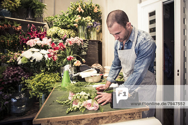 Mittlerer erwachsener männlicher Florist mit Blumenstrauß am Schreibtisch im Geschäft