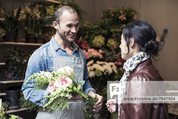 Fröhlicher männlicher Florist  der dem Kunden im Geschäft einen Blumenstrauß schenkt.