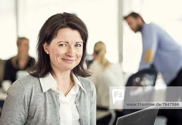Porträt einer mittleren erwachsenen Frau mit Kollegen im Hintergrund im Büro