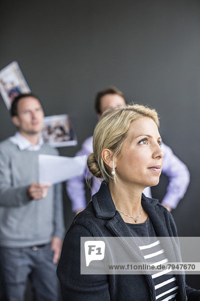 Mittlere erwachsene Geschäftsfrau schaut mit Kollegen weg  die im Hintergrund diskutieren.
