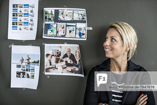 Mid adult businesswoman smiling while looking at photographs on wall in office