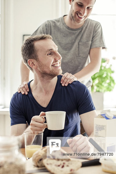 Young gay man massaging partner having breakfast at table