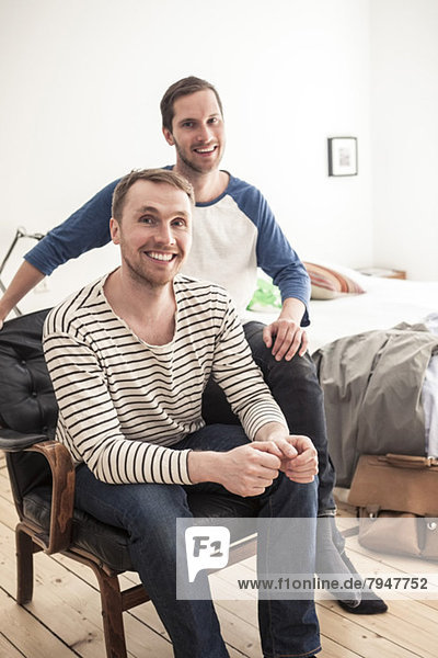 Porträt eines glücklichen homosexuellen Paares  das auf einem Stuhl im Schlafzimmer sitzt.