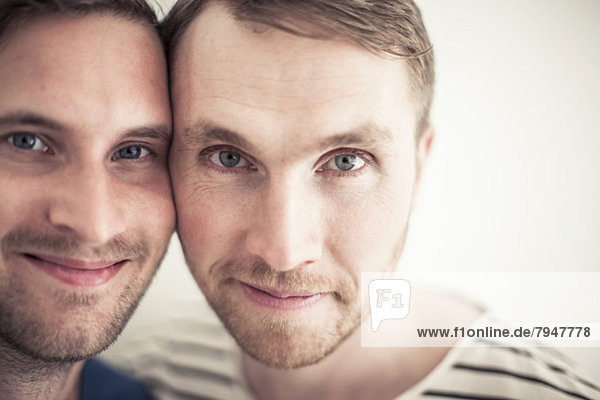 Porträt eines jungen homosexuellen Paares,  das Wange an Wange lächelt.