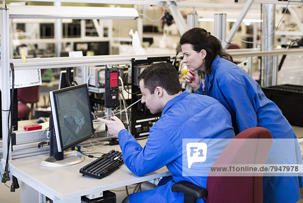 Male electrician pointing at computer monitor while discussing with colleague in industry