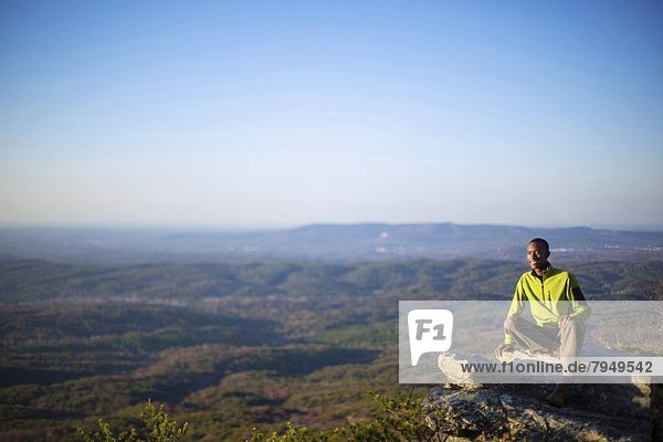 A young man sits on the ledge of a rock overlook on top of Mount Cheaha.