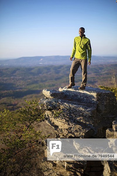 A young man stands on boulder on the edge of Mount Cheaha