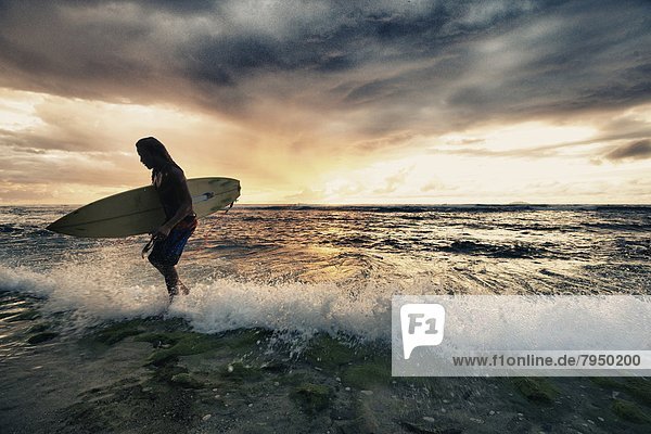 Surfer exiting water with surfboard at sunset in Rincon  Puerto Rico