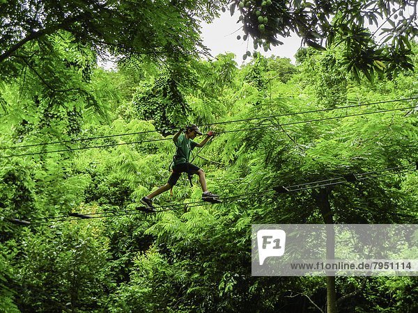 Young boy strecthing across a ropes course high in the jungle of Saint Martin in the Caribbean.