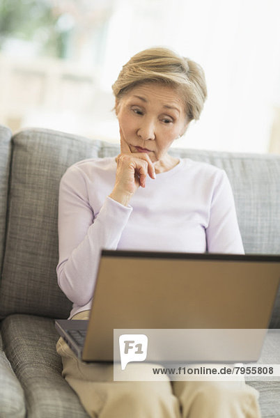 Senior woman sitting on sofa and using laptop