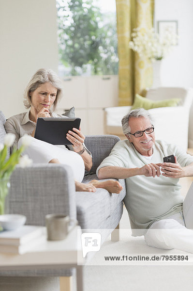 Senior couple using digital tablet and cell phone at home