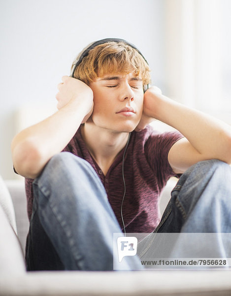 Teenage boy (14-15) sitting on bed with headphones and closed eyes