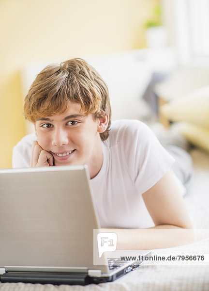Teenage boy (14-15) lying on bed and using laptop