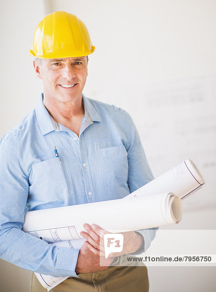 Portrait of man in hardhat holding rolled up blueprints