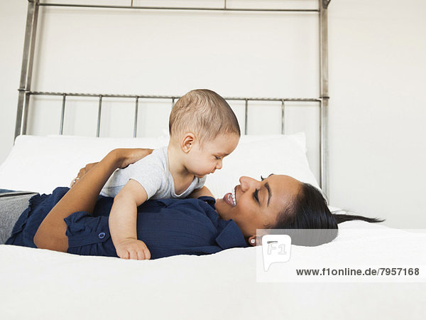 Mother holding her son (2-5 month)  lying in bed happily