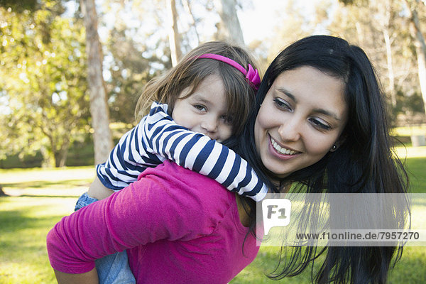 Portrait of mother giving her daughter (4-5) piggy back ride in park