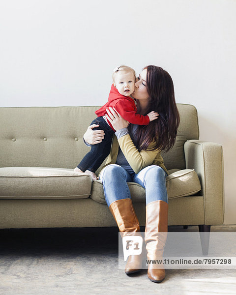 Portrait of mother sitting on sofa and kissing her daughter (12-17 months)