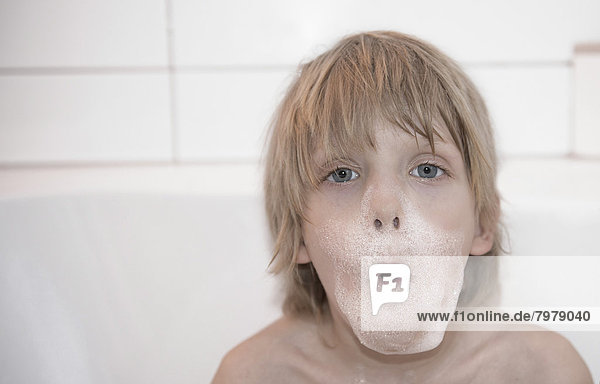 Österreich  Junge sitzend in Badewanne mit Schaumstoff im Gesicht