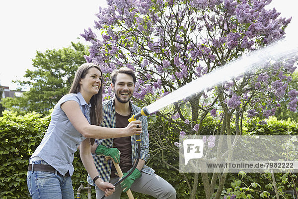 Germany  Cologne  Young couple watering garden  smiling