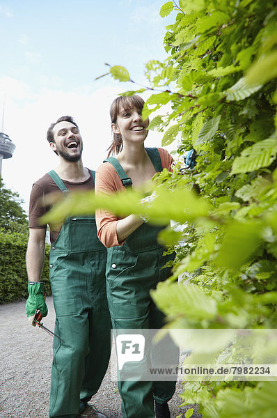 Deutschland  Köln  Junges Paar  das mit einer Schere Blätter schneidet  lächelt