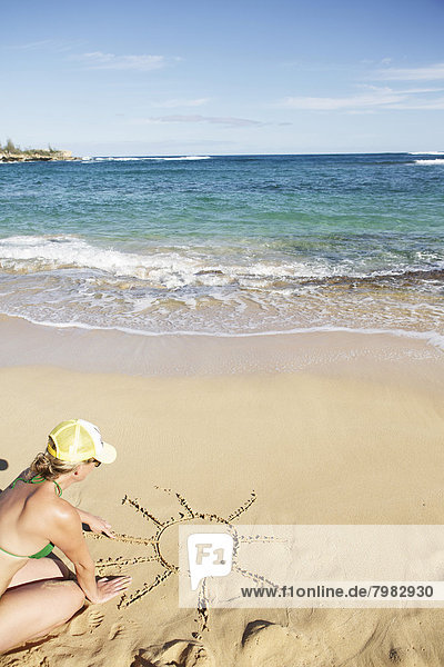 USA  Hawaii  Mittlere erwachsene Frau zeichnet Sonne auf Sand