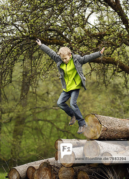 Deutschland  Baden Württemberg  Junge springt aus Holzstämmen