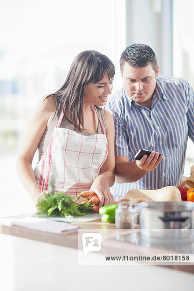 Paar  das während der Zubereitung des Essens auf das Smartphone schaut