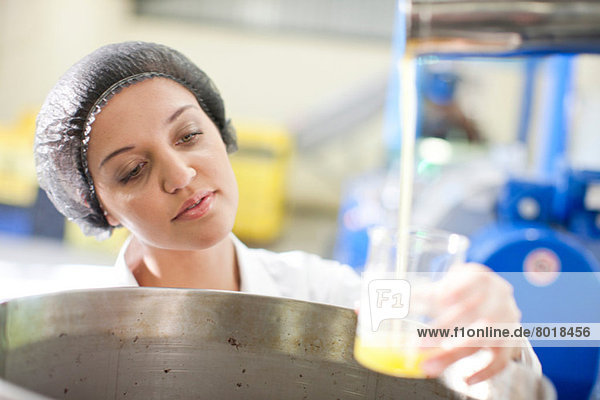 Woman holding beaker of olive oil in olive processing plant