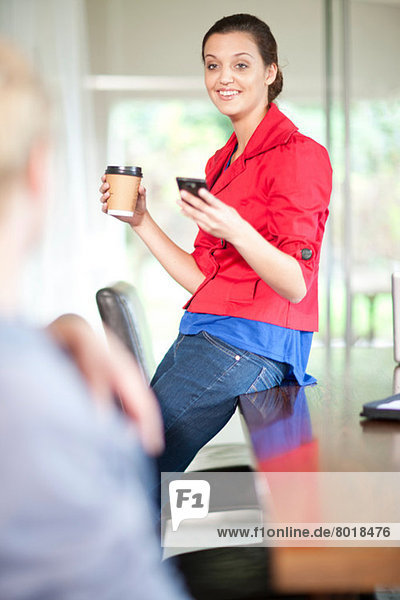 Junge Frau im Büro mit Handy und Kaffee
