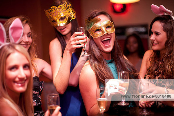 Junge Frauen mit Getränken in Masken auf der Junggesellinnenparty