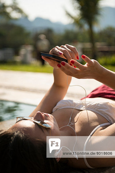 Woman sunbathing on poolside listening to music