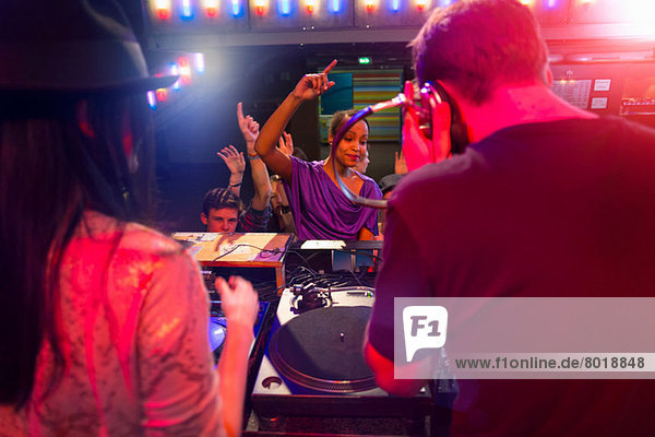 Rear view of disc jockey surrounded by people dancing