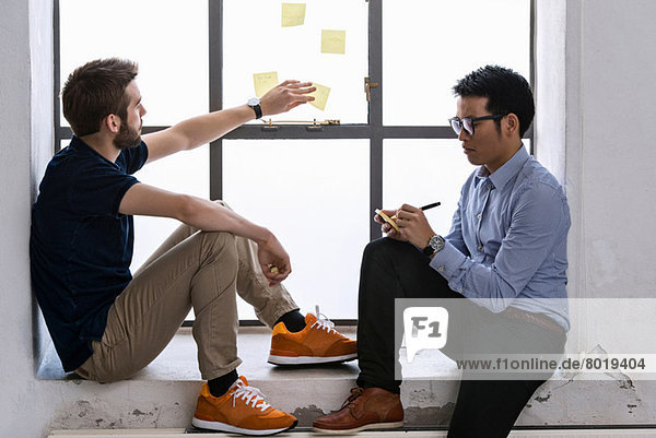 Two young male designers sharing ideas on post it notes