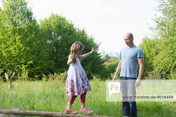 Father watches daughter balancing on tree trunk