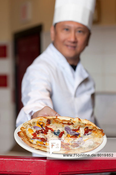 Mature chef holding fresh pizza on plate  portrait