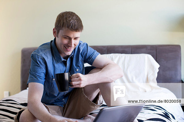 Mid adult man sitting on bed using laptop
