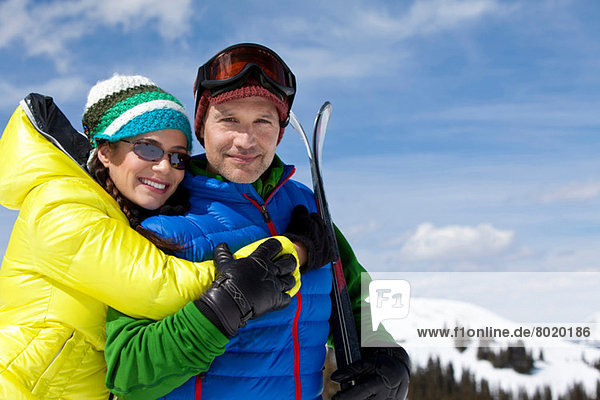 Junge Frau in Skibekleidung umarmt reifen Mann mit Skiern  Portrait