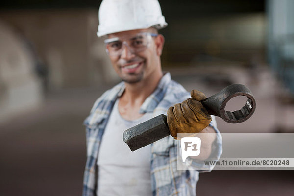 Mid adult construction worker wearing hard hat and holding wrench  portrait