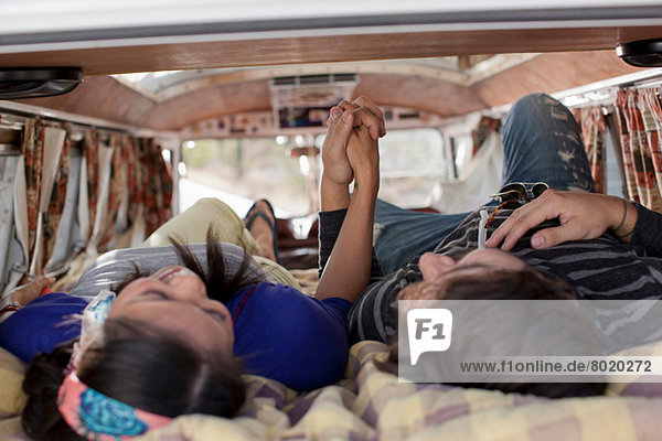 Couple lying together in the back of camper van  holding hands